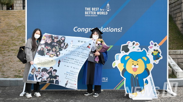 17日，在首尔城东区首尔校区里，毕业生拿着朋友制作的横幅，以拍照区为背景拍摄着纪念照片。