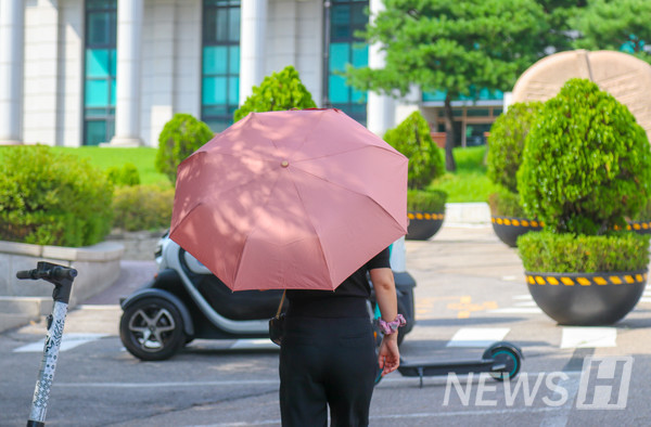 ▲ 한 여성이 뜨거운 햇빛을 피하기 위해 양산을 쓰고 언덕을 오르고 있다.
