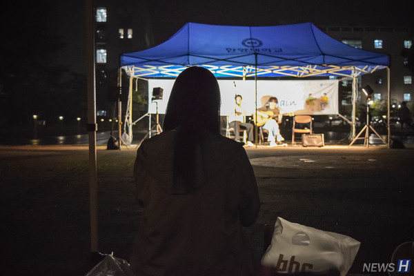 ▲ 학생이 관람객용 천막 아래에서 비를 피하며 버스킹을 감상하고 있다.