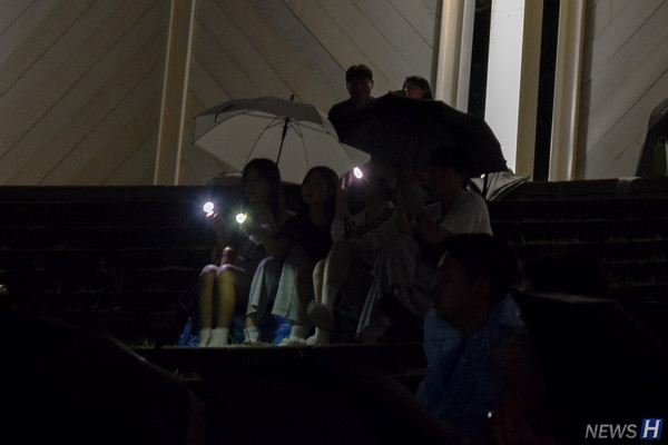 ▲ 버스킹 중 쏟아지는 비에 우산을 쓰며 관람하고 있다.