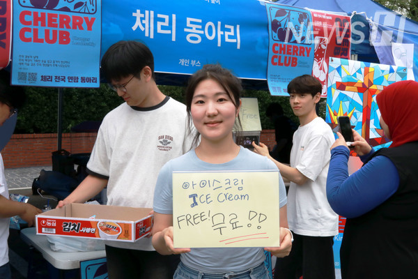 ▲ A 토토사이트 사고 팔고 organizer from the Cherry Club explains the giveaway event with a sign