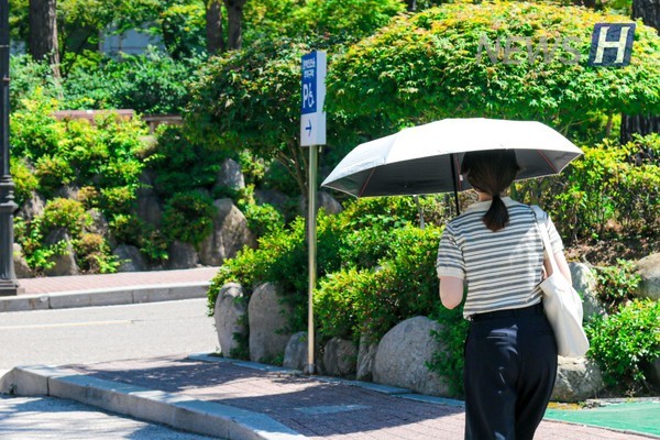 ▲ A student opens a parasol to shade themselves from the strong midday sun.