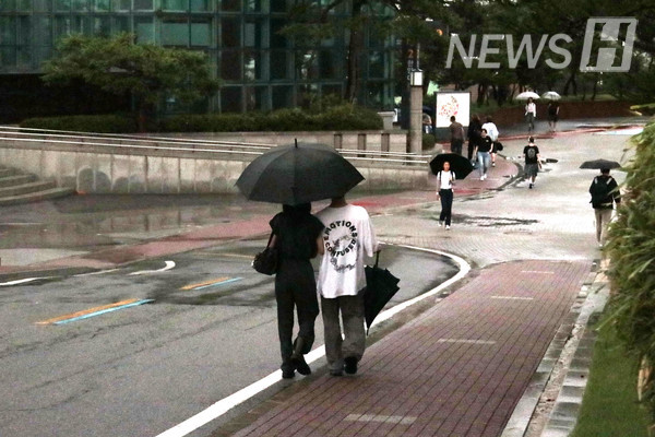 ▲ 두 학생이 우산을 나눠쓰고 빗속을 걷고 있다.