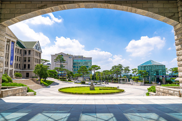 A glimpse of the Hanyang University History Museum through an arch, framed by the blue sky and the fresh greenery of summer.