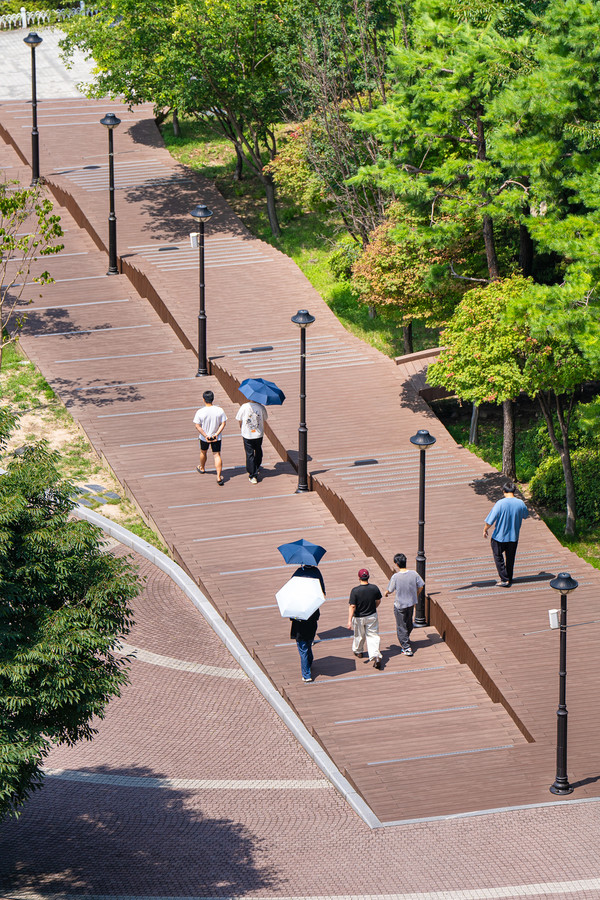People walk along the trail, shielding themselves from the summer sun with umbrellas.