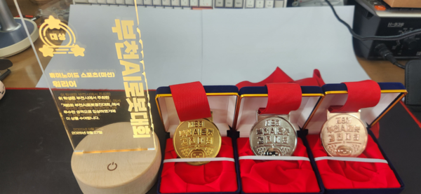 덕일전자공업고등학교 학생들의 수상 내용. 왼쪽부터 미션-워리어 부문 대상 트로피, 스프린트 부문 금상, 스프린트 부문 은상, AI자율주행 파트 동상 메달이다.