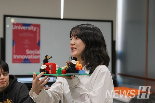 ▲ A participant holds the model and explains her 'Social Innovation University' idea. 