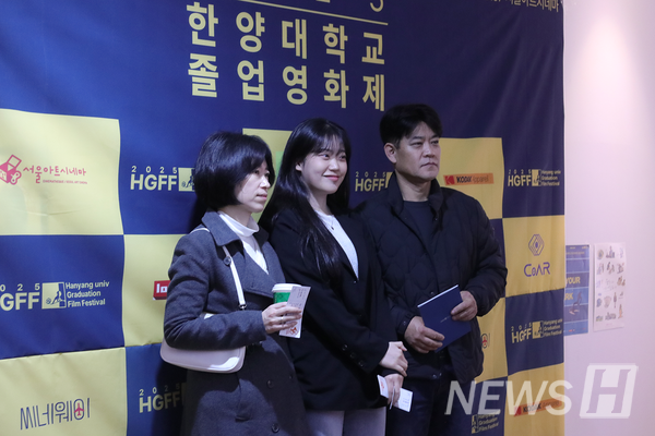 ▲ A student takes a commemorative photo with their parents in front of the photo wall.